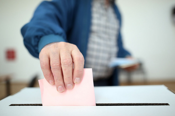 Ein Mann steckt einen gefalteten Zettel in einen Wahlurne
