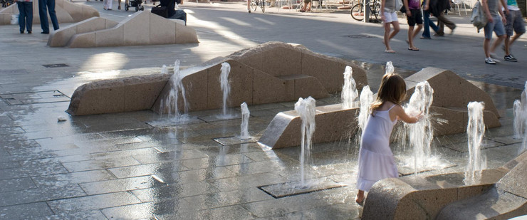 Kind spielt mit sprudelndem Wasser in einer Fußgängerzone der Leipziger Innenstadt