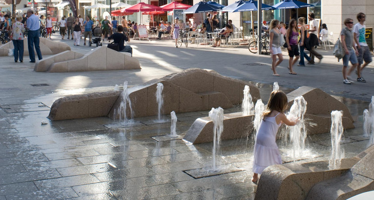 Kind spielt mit sprudelndem Wasser in einer Fußgängerzone der Leipziger Innenstadt
