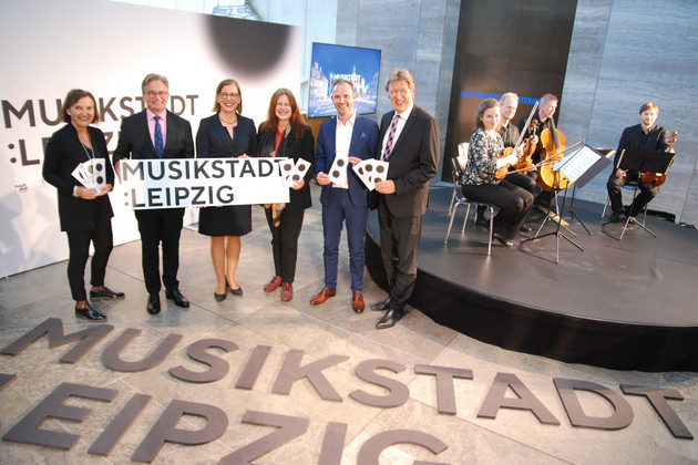 Mehrere Menschen stehen vor einem großen Logo und präsentieren den Schriftzug "Musikstadt Leipzig"