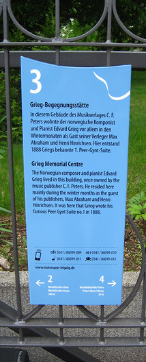 Schild der Leipziger Notenspur zur Grieg-Begegnungsstätte an einem Metalzaun.