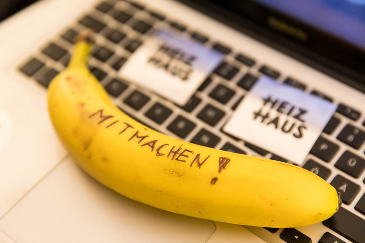 Auf einer Laptoptastatur kleben Klebezettel mit dem Titel "Heizhaus" drauf. Außerdem liegt eine Banane auf der Tastatur auf der Mitmachen! geschrieben steht.
