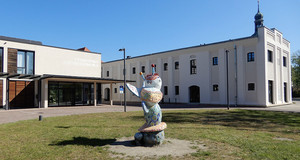 Mit Mosaiksteinen gestaltete Raupen- und Schmetterlingsskulptur auf eine Wiese vor der Förderschule Schloss Schönefeld.