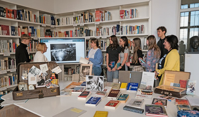 Eine Gruppe Jugendlicher in einer Bibliothek betrachtet ein historisches Foto der Bücherverbrennung auf einem Bildschirm