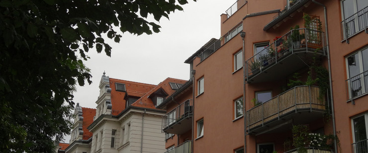 Häusergiebel in der Weinligstraße Gohlis, ein sanierter Altbau in weiß, ein Neubau in rot, rechts im Vordergrund Blätter von einem Baum