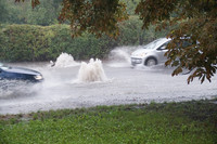 Zwei Autos fahren auf einer von Starkregen überfluteten Straße. 