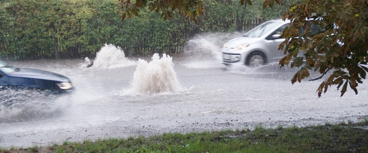 Zwei Autos fahren auf einer von Starkregen überfluteten Straße.