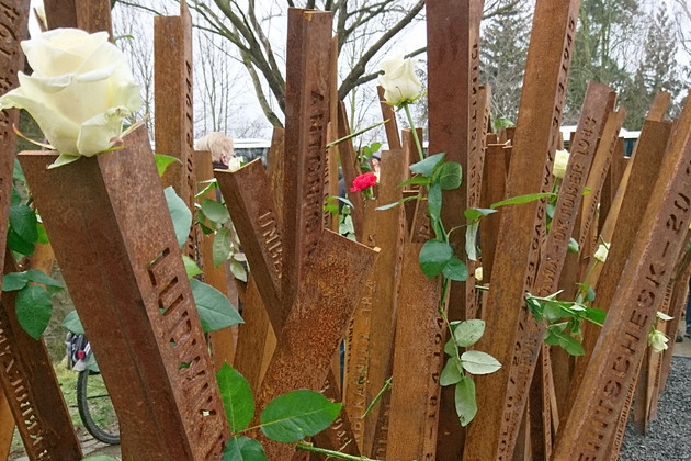 Rostige Stahlwinkel, in die die Namen und Lebensdaten der Opfer des KZ Außenlagers in Abtnaundorf eingeschnitten sind. Einige sind mit weißen Rosen geschmückt.