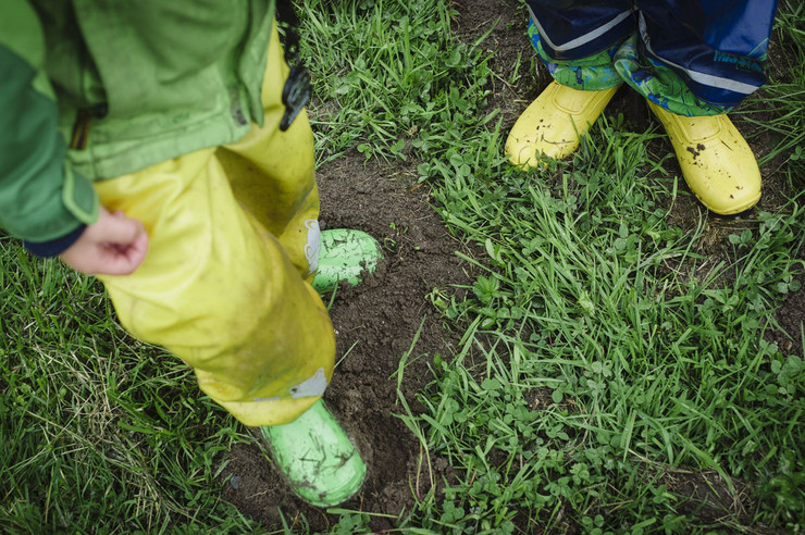 Die Beine von zwei Kinden mit Gummistiefeln und Regenhose auf einer nassen Wiese