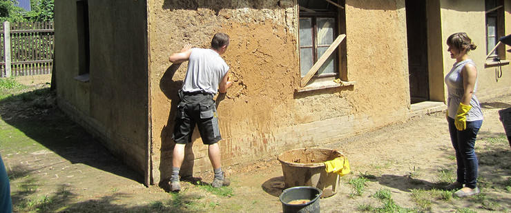2 Menschen reparieren die Lehmwand an einem denkmalgeschützem Haus.