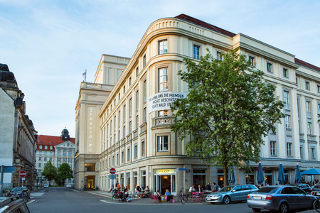 Außenansicht des Schauspiels Leipzig. Im Vordergrund eine Straßenkreuzung, dahinter das Schauspiel Leipzig, ein mehrstöckiges altes Gebäude aus Sandstein.