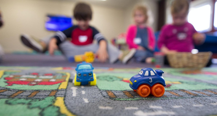 Spielende Kinder auf einem Teppich mit Straßen, darauf sind kleine Spielzeugautos.