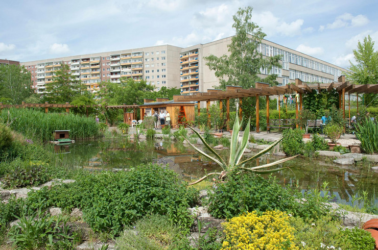 Im Vordergrund ist der Kolonnadengarten im Wohnkomplex 2 in Grünau zu sehen, im Hintergrund sind Plattenbauten. 