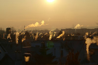 Stadt bei Sonnenuntergang mit mehreren rauchenden Schornsteinen