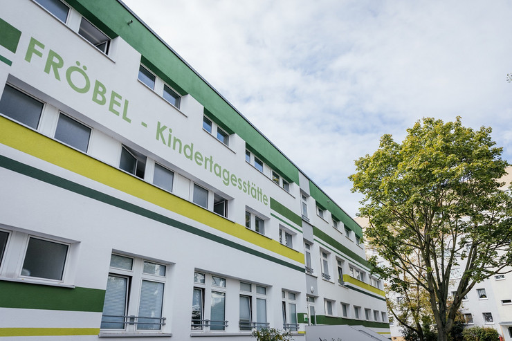 Weißes Gebäude mit grünen und gelben Absätzen der Fröbel-Kindertagesstätte.