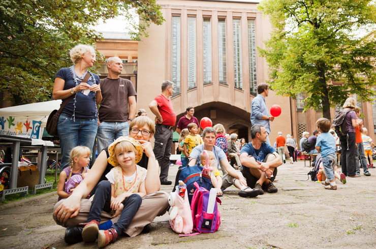 Viele Erwachsene und Kinder im Innenhof des Grassimuseums, einige sitzen, einige stehen. Manche haben rote Luftballons in der Hand.