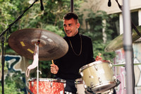 Ein junger Mann mit kurzen dunklen Haaren sitzt lächelnd an einem Schlagzeug
