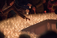 Eine große Fläche aus mit Kerzen gefüllten Gläsern. Eine Frau stellt ein weiteres dazu.