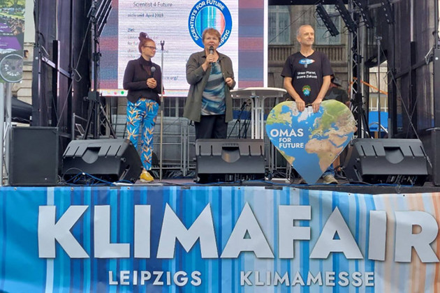 Bühne der Klimamesse "Klimafair" mit drei Personen, die zum Thema Klimaschutz sprechen