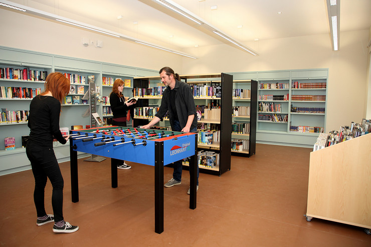 Jugendbereich der Bibliothek Plagwitz mit Einbauregalen in den Wänden, im Vordergrund ein einem Kickertisch, zwei Personen spielen.