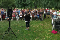 mehrere Menschens stehen im Halbkreis und singen im Park