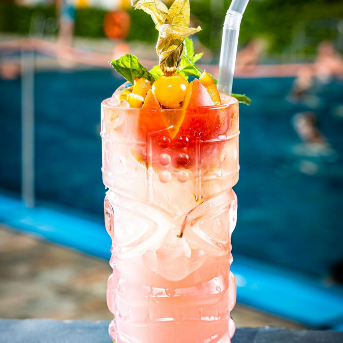 blass rosafarbener Cocktial in Glas in Maskenform, dekoriert mit sternförmiger angeschnittener Passionsfrucht und Physalis