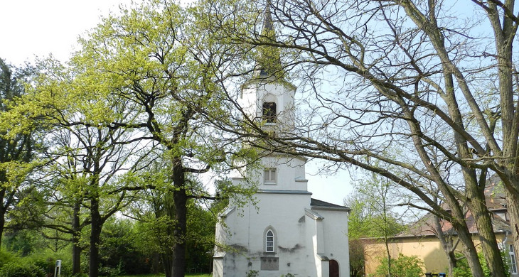 Eine kleine weiße Kirche umgeben von Wiese und Bäumen