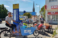 Drei Menschen sitzen auf Lastenrädern an einer Mobilitätssäule mit der Aufschrift Leipzig Move.