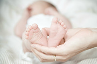 Symbolbild Geburt: Ein Neugeborenes liegt auf dem Rücken. Eine Hand hält die zwei kleinen Füße des Babys in die Kamera.