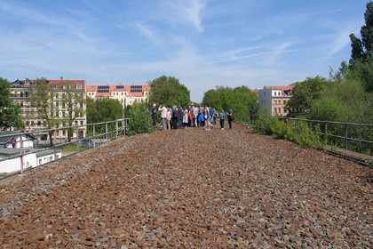 Eine Gruppe Menschen steht einer ehemaligen Bahnbrücke, die noch mit Steinen des Gleisbetts gefüllt ist.