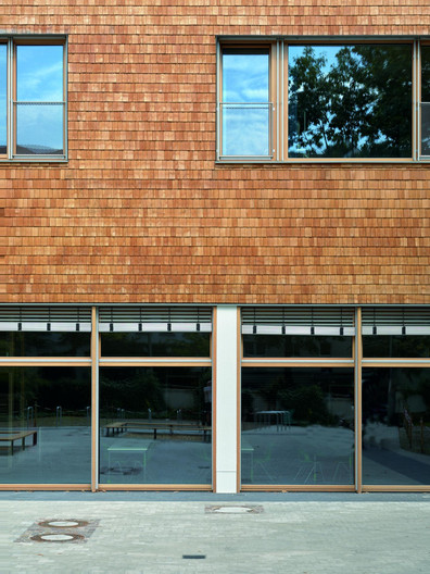 Detailansicht des Erweiterungsbau mit einer Fassade aus Lärchenholzschindeln und Verglasung im Erdgeschoss.