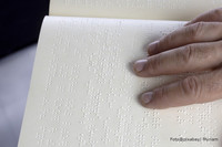 Weißes Blatt Papier mit gestanzten Punkten, die von einer Hand ertastet werden