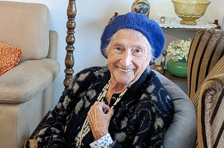 Eine alte Frau sitzt auf einem Sessel und lächelt in die Kamera.