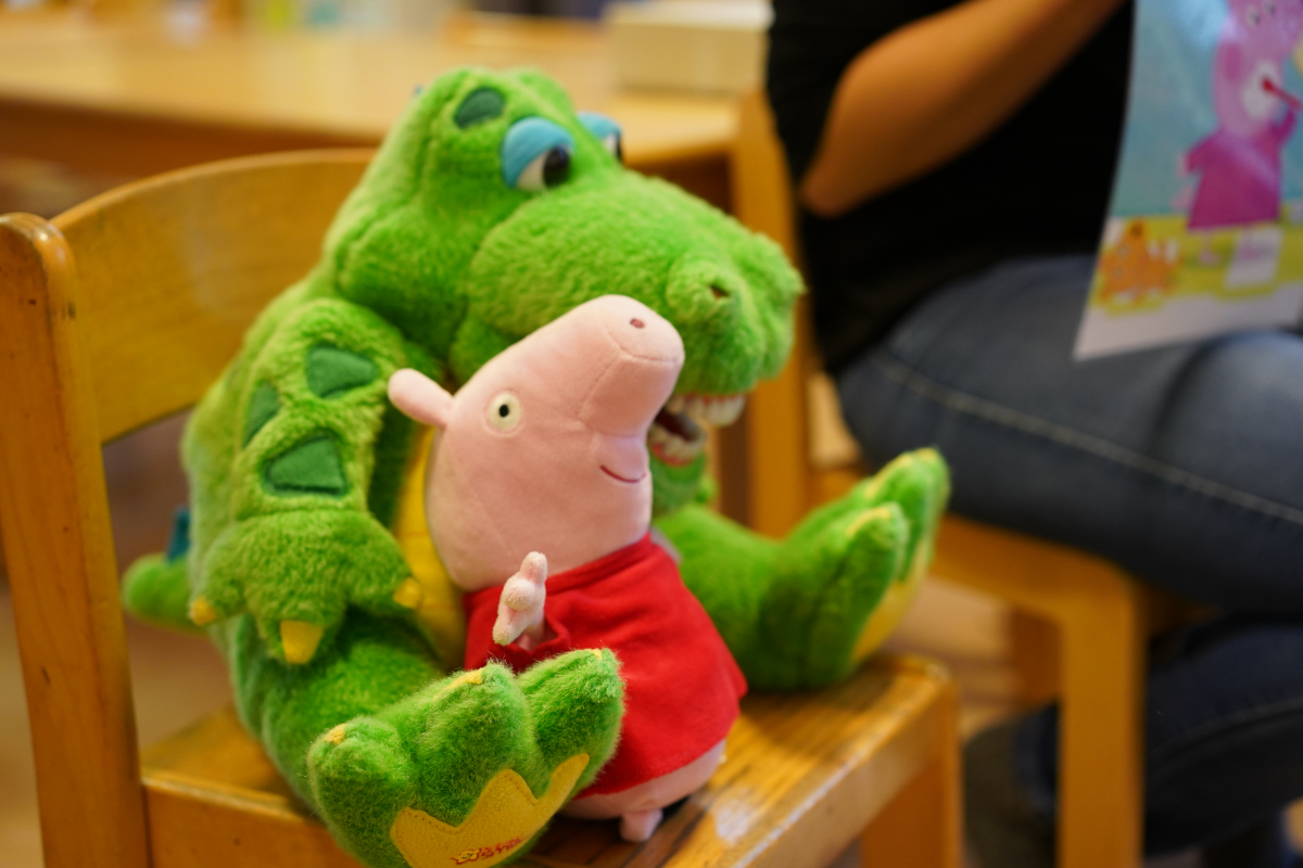 Ein kleines Plüschschweinchen und ein grünes Zahnputzkrokodiel sitzen auf einem Kinderstuhl